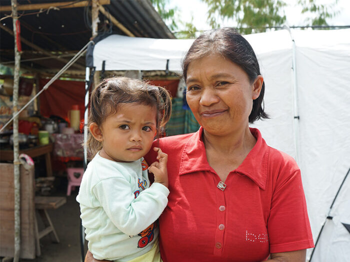 Eine Frau mit Kind im Arm steht vor einem Zelt in Indonesien