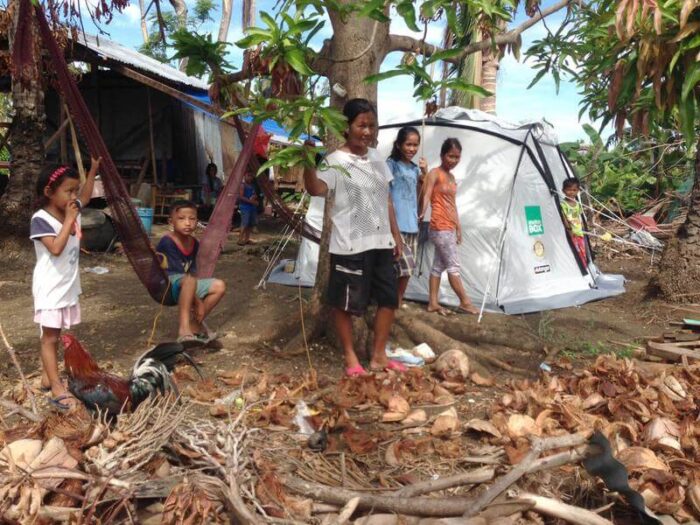 Eine Familie in den Philippinen steht nach dem Taifun Haiyan unter Bäumen neben einem ShelterBox Zelt