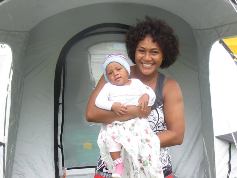 Eine Frau mit Kind steht vor einem ShelterBox Zelt