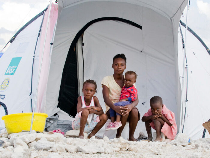 Mutter und Kinder sitzen vor ihrem ShelterBox Zelt in Haiti