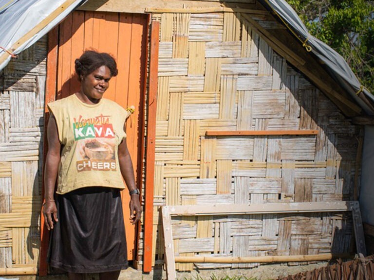 Eine Frau steht vor ihrem Zuhause in Vanuatu