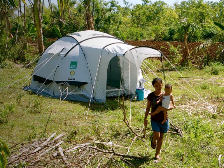 woman carrying baby in front of shelterbox tent in the philippines