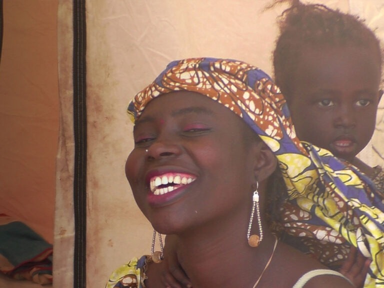 Eine lächelnde Frau mit Kopfbedeckung und einem Kind, das hinter ihr steht in Kamerun