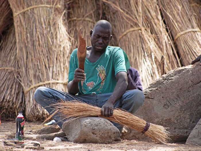 Ein Nigerianer sitzt auf dem Boden und fertigt aus getrocknetem Gras eine Kehrbürste an.