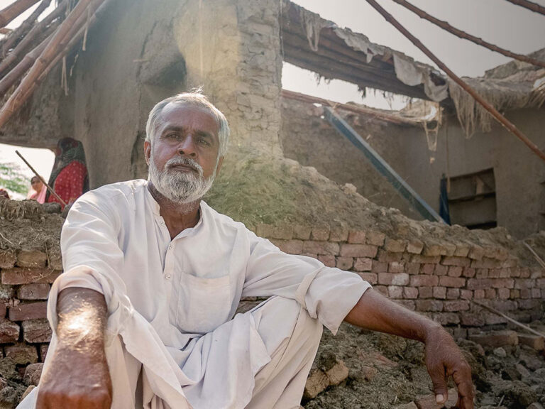 Ein Mann in Pakistan sitzt vor seinem Zuhause, das von Überschwemmungen zerstört wurde