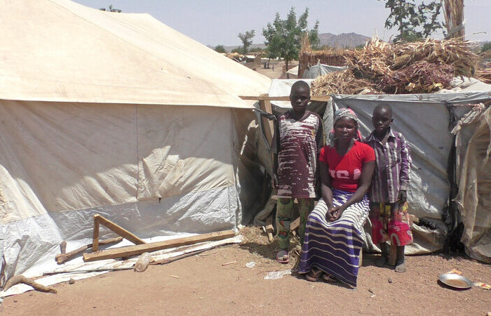 Eine Frau und Kinder stehen und sitzen vor einem Zelt in Kamerun