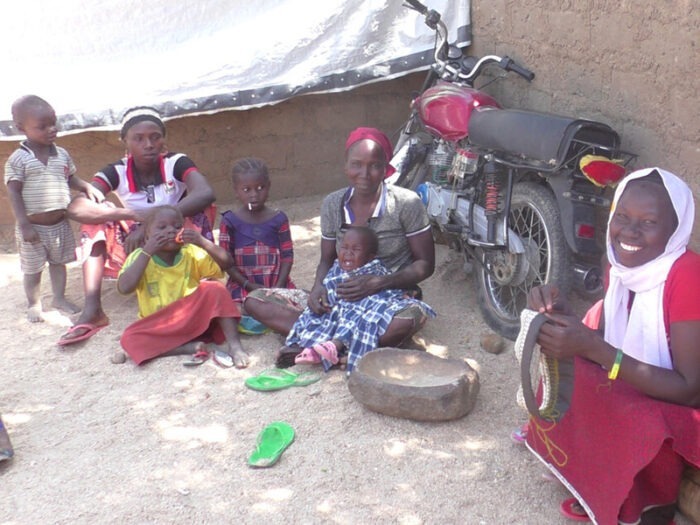 Eine Frau sitzt mit ihrer Familie und bestickt einen Hut