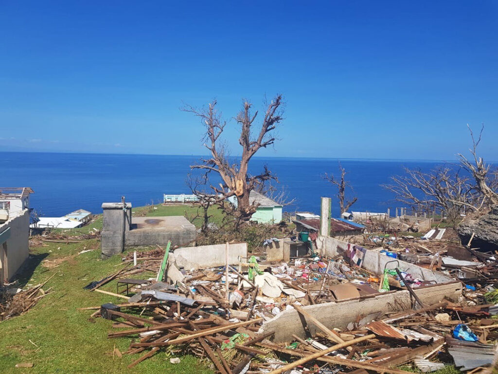 Trümmer eines zerstörten Hauses neben einem Baum vor dem Hintergrund eines blauen Himmels und dem Meer