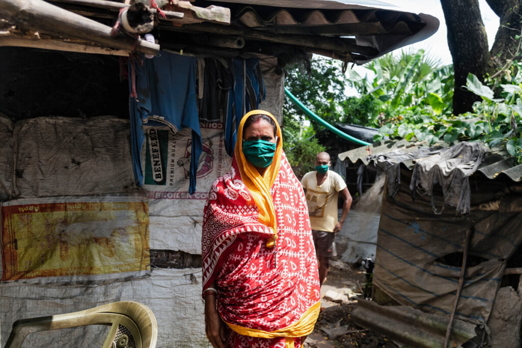 Frau mit buntem Kopftuch und Gesichtsmaske neben einer Unterkunft in Indien