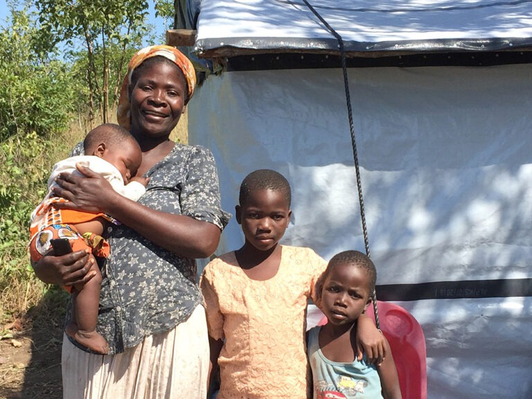 Eine Mutter und drei Kinder stehen vor einer reparierten Unterkunft in Malawi.