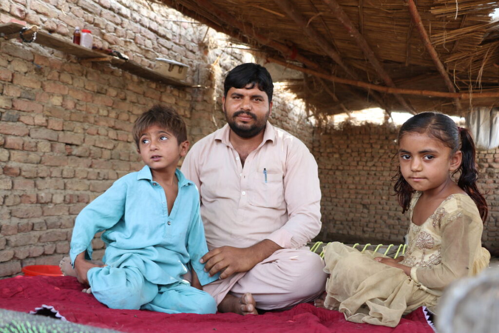 Ein Mann sitzt mit zwei Kindern auf dem Boden einer Unterkunft in Pakistan