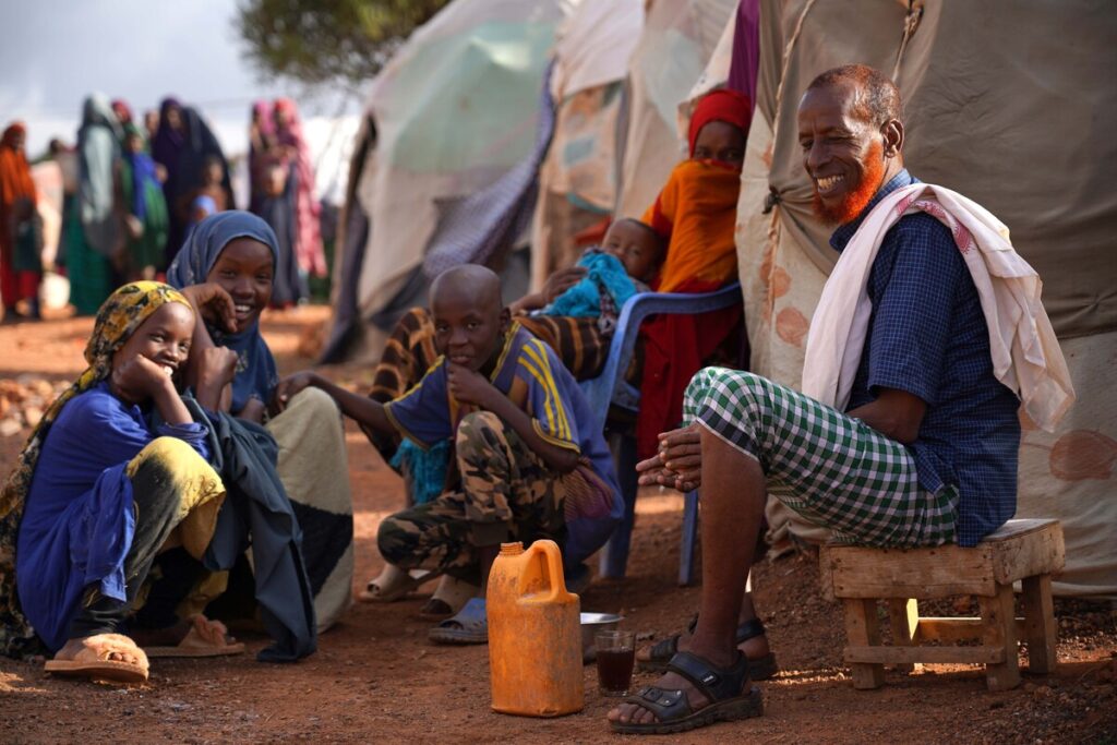 Ein lächelnder Mann sitzt, von Kindern umgeben, vor einem Zelt in Somalia
