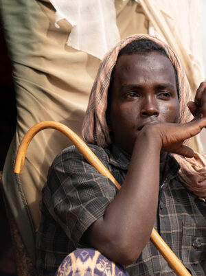 Man holding a stick sitting outside of a shelter