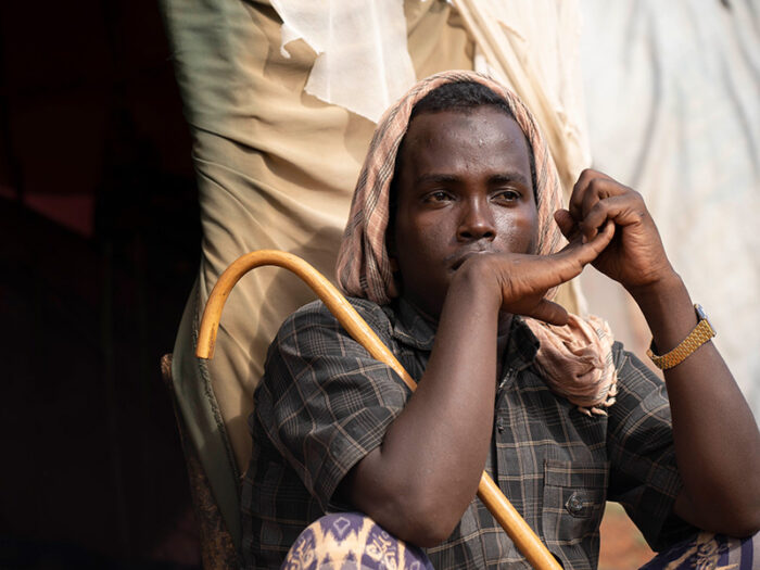 Man holding a stick sitting outside of a shelter