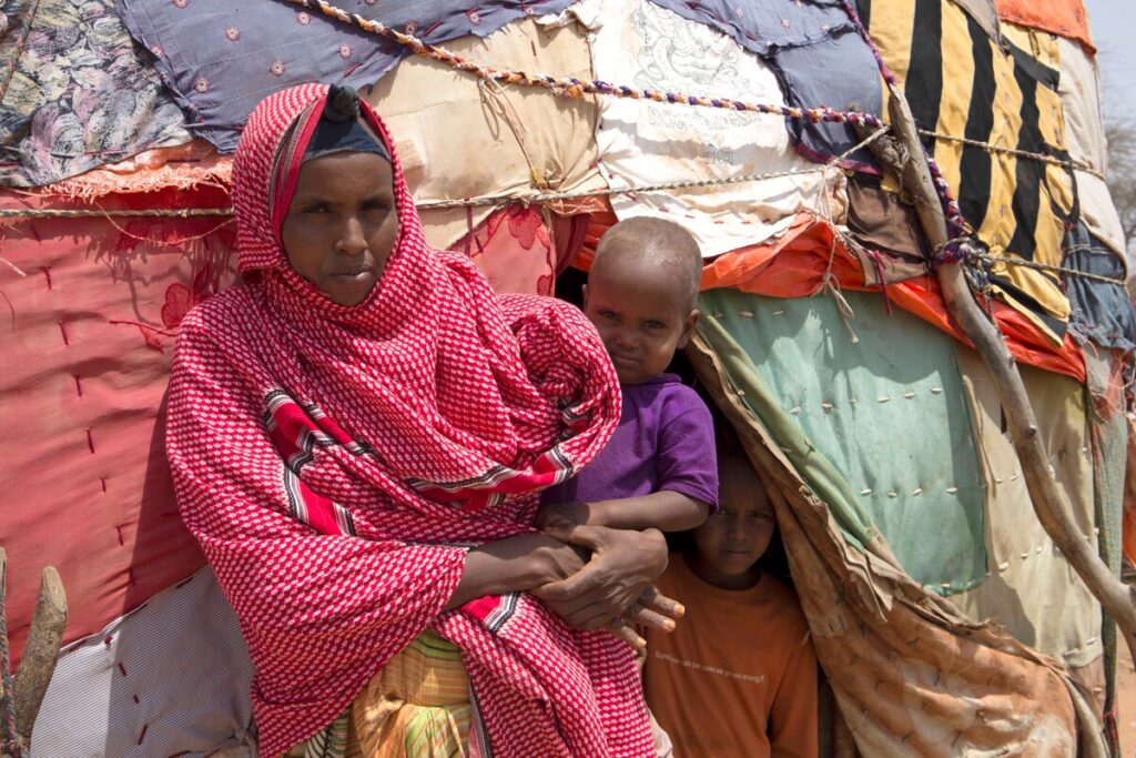 Eine Frau mit Kind im Arm steht vor einer vorübergehenden Unterkunft in Somaliland