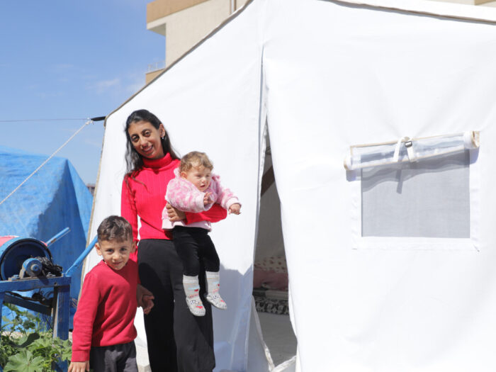 Frau mit einem Baby im Arm und einem Kind an der Hand neben einem Zelt in der Türkei