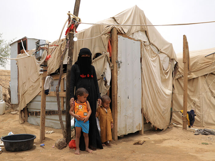 Woman and two children standing outside a temporary shelter in Yemen