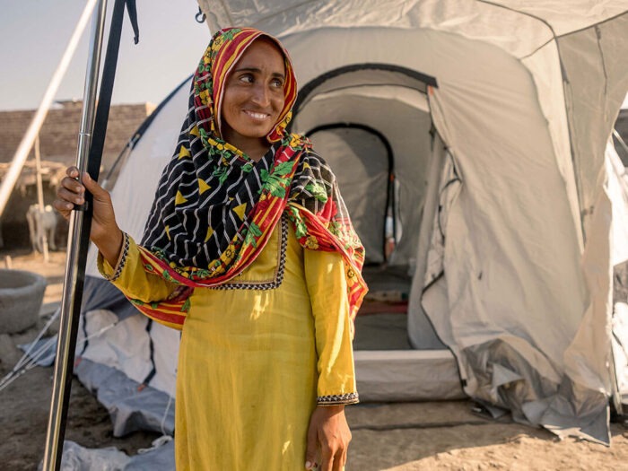 Eine Frau in gelber Kleidung lächelt vor einer Notunterkunft in Pakistan