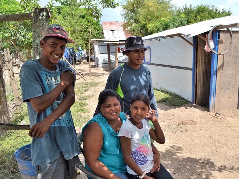 Eine Frau sitzt mit ihren drei Kindern neben Unterkünften in Honduras