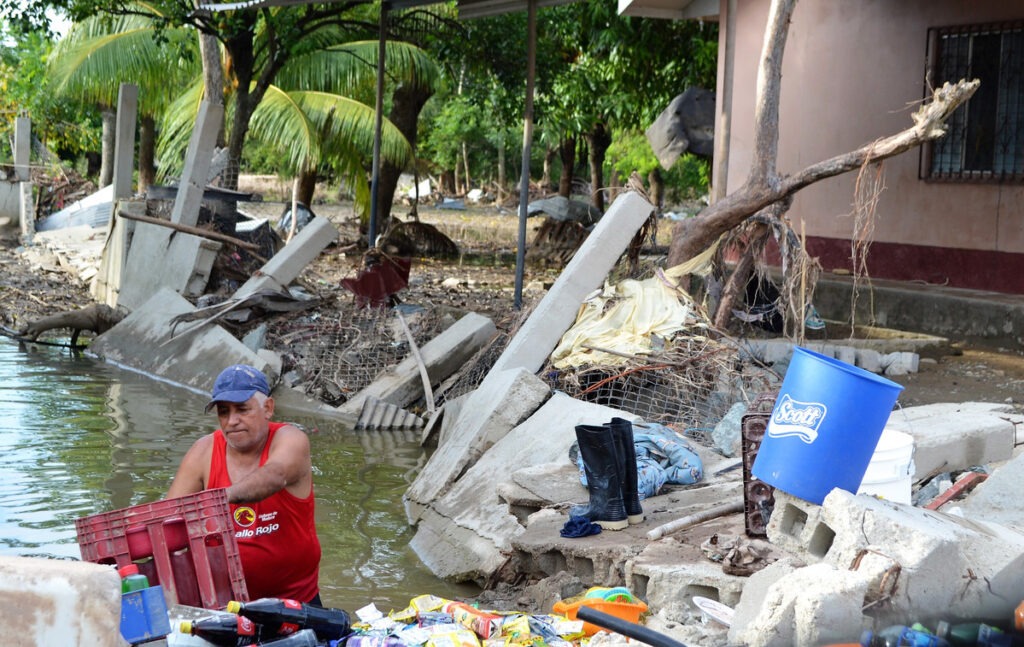 Ein Mann rettet Habseligkeiten aus einem beschädigten Gebäude, während er in Honduras nach den Hurrikanen im Jahr 2020 im Hochwasser steht.