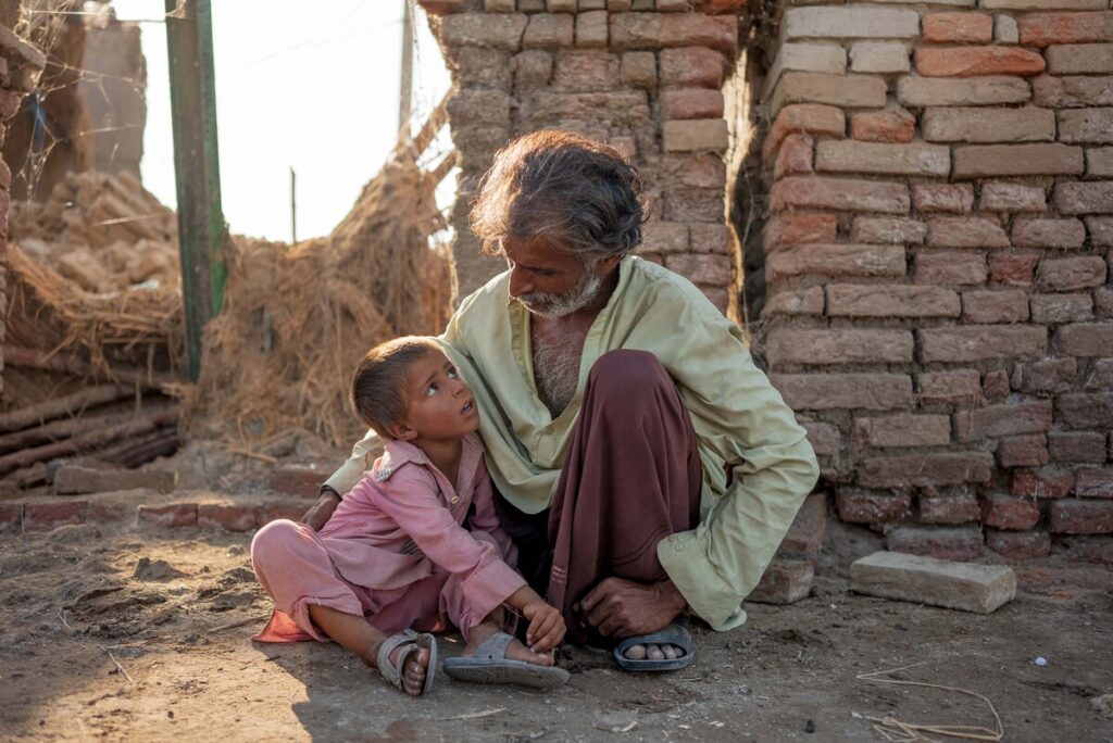 Ein Mann und ein Kind sitzen zwischen von Überschwemmungen zerstörten Gebäuden auf dem Boden in Pakistan