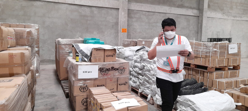 Mann mit Gesichtsmaske, der telefoniert und in einem Lagerhaus von ShelterBox Operations Philippines Unterlagen durchsieht.