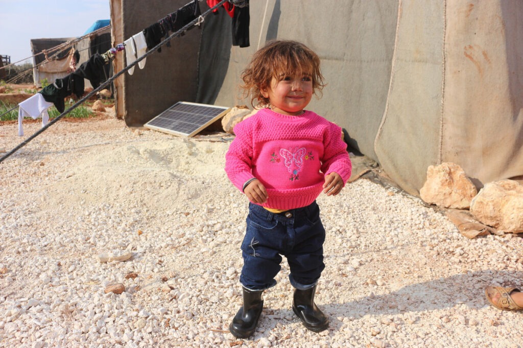 Ein Kind in warmem, pinken Pullover in einem Vertriebenenlager in Syrien