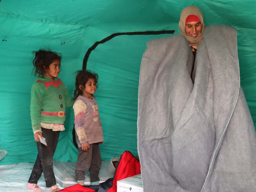 Eine Frau und ihre Kinder stehen in einem Zelt in Syrien. Sie hält eine Decke hoch