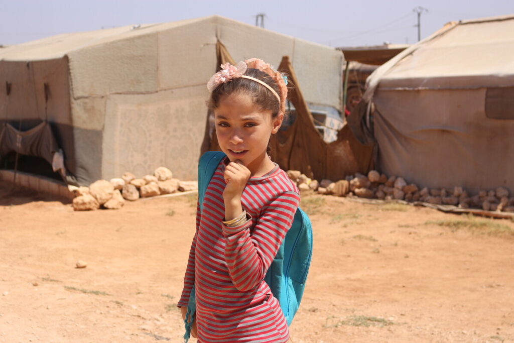 Ein Mädchen trägt einen Schulrucksack vor Zelten in Syrien