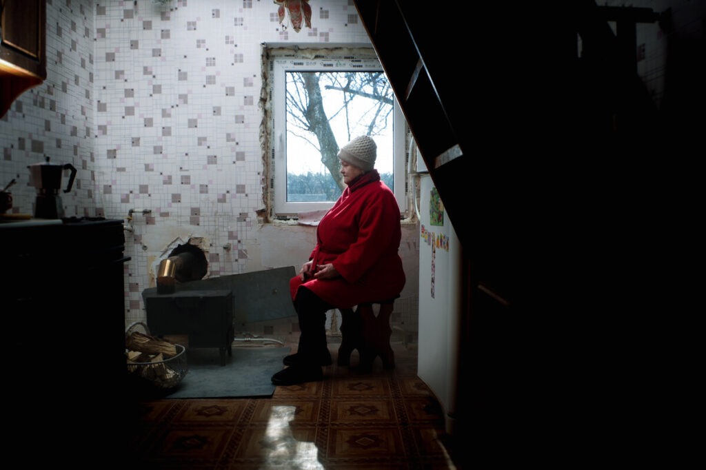 Eine Frau sitzt in einem beschädigten Gebäude mit einem Ofen in der Ukraine