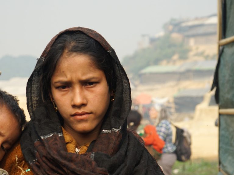 Eine junde Frau hält ein Kind inmitten von Unterkünften in Bangladesch