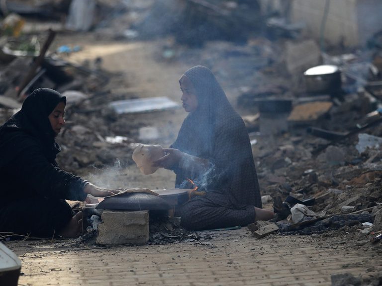 Zwei Frauen sitzen auf der Straße, nachdem sie ihr Zuhause in Gaza verloren haben