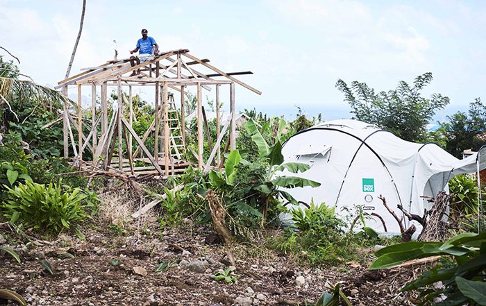 Man on top of timber frame for a building next to a ShelterBox tent