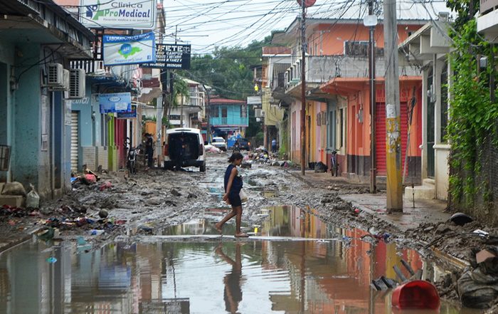 Frau läuft durch eine überflutete Straße zwischen beschädigten Gebäuden in Honduras