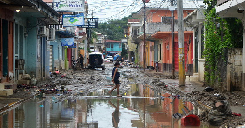Frau läuft durch eine überflutete Straße zwischen beschädigten Gebäuden in Honduras