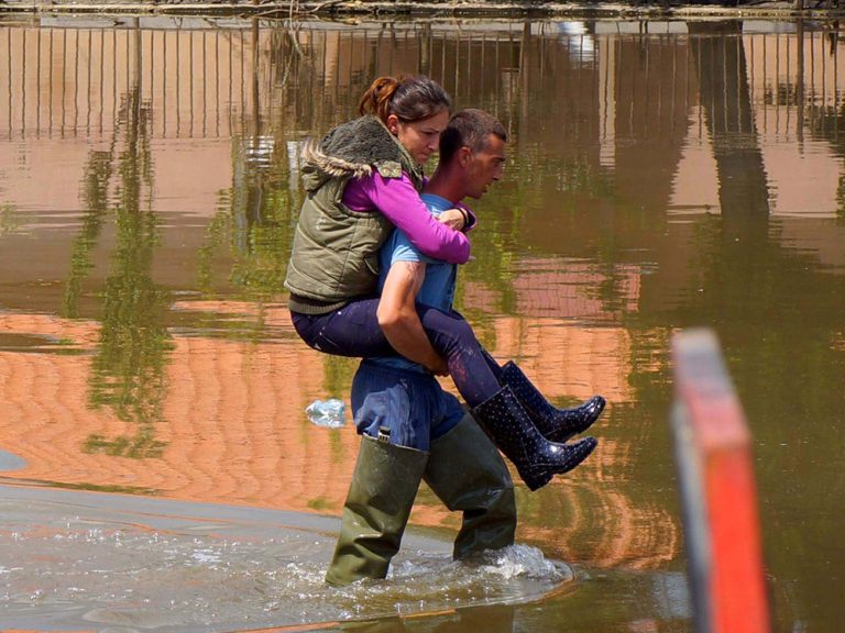 Ein Mann trägt eine Frau auf dem Rücken und watet durch Überschwemmungen in Serbien