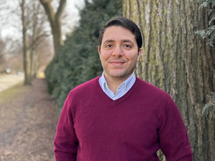 Ein Mann in rotem Pullover steht neben einem Baum