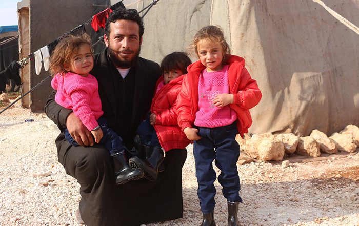 Man and three children wearing winter coats next to tents in Syria
