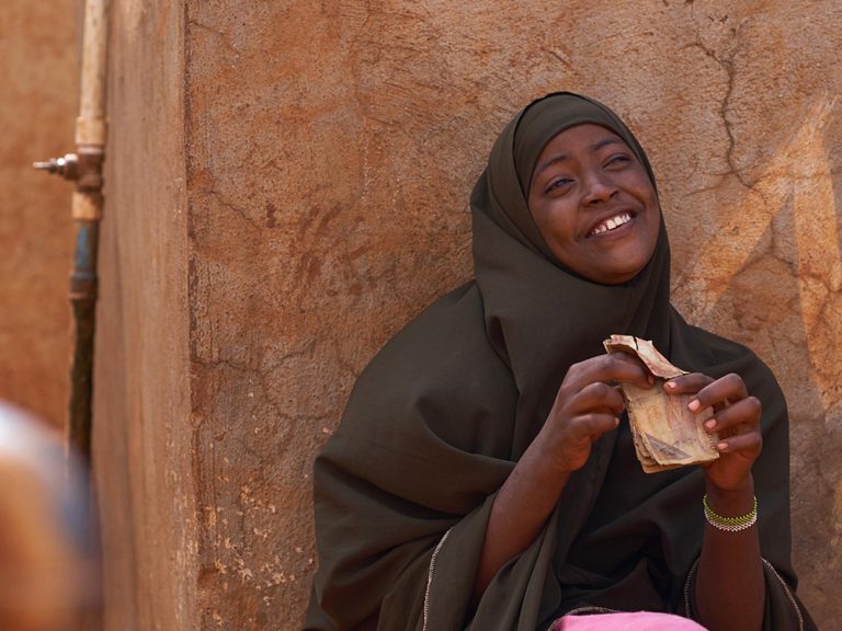 Eine Frau sitzt lächelnd neben ihrer Unterkunft in Somalia