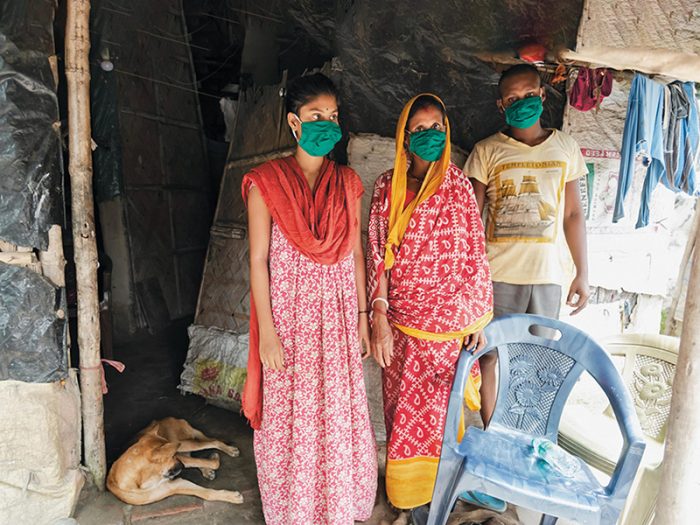 Drei Menschen mit Mundschutz stehen in ihrem Zuhause in Indien